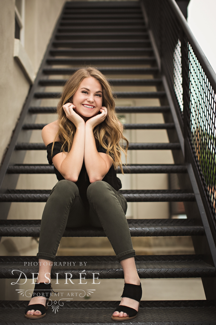 cute high school senior girl sitting on stairs hands around her face