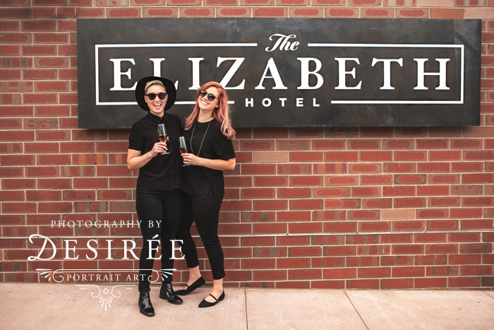 cute couple standing in front of the elizabeth hotel sign with champagne