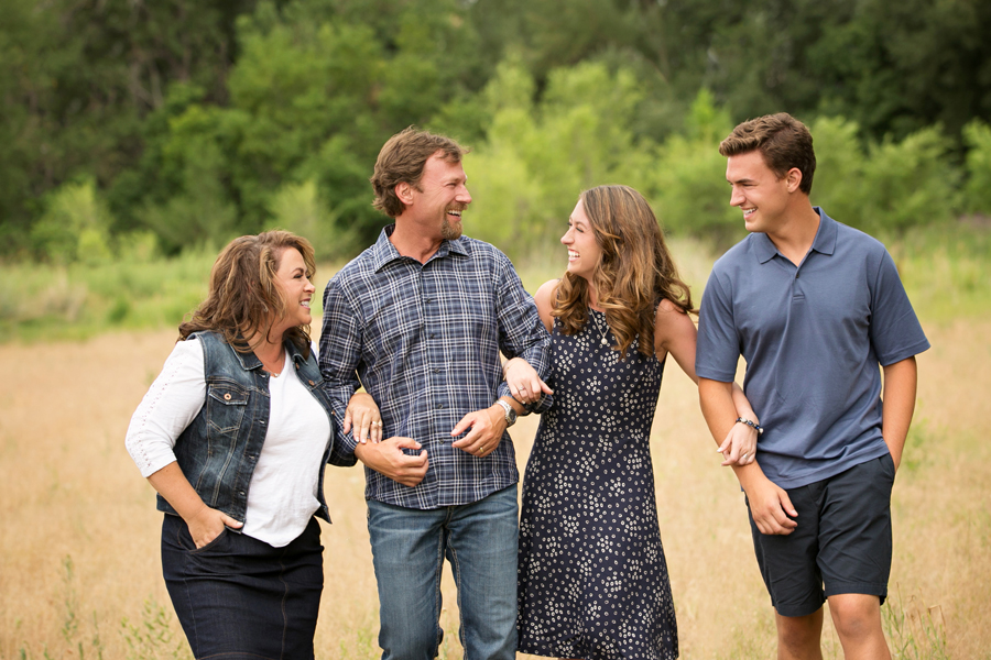 family of four candid laughing at each other with linked arms walking through field