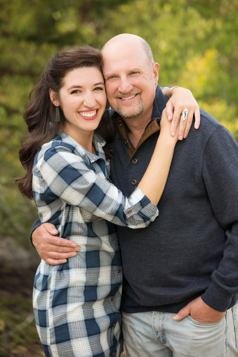 father and adult daughter hugged smiling at camera with fall backdrop