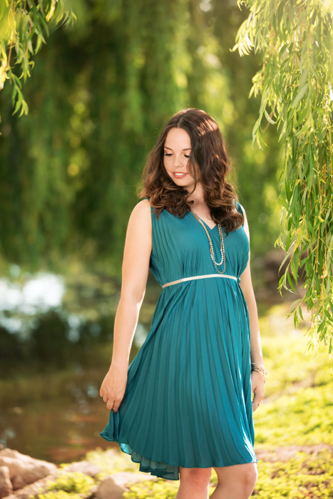 young woman by willow tree swinging dress and looking down