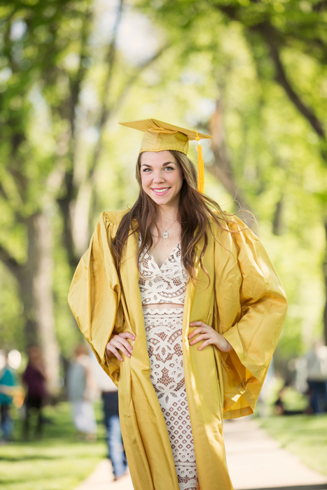college grad girl in white lace dress and gold robes with hands on hips