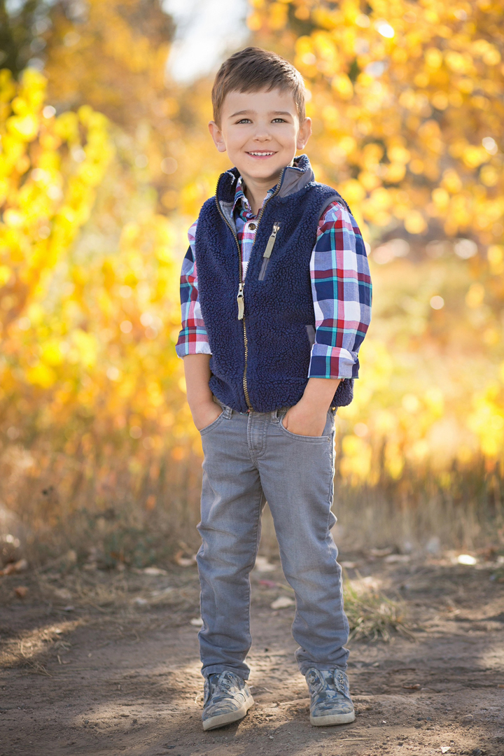 Portrait of a little boy with a vest and plaid shirt, full length in front of bright yellow Aspen leaves taken in the fall at The Rock Garden