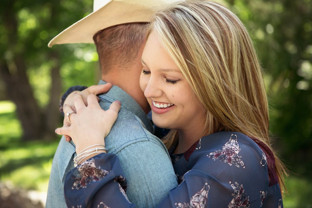 Engagement portrait of a young woman and her cowboy hugging showing her engagement ring at Gateway Natural Area in Colorado
