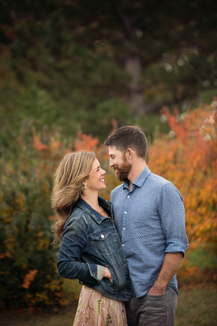 Couple in Boulder, Coloardo looking at each other and smiling with a background of red and yellow foliage from the fall photo session