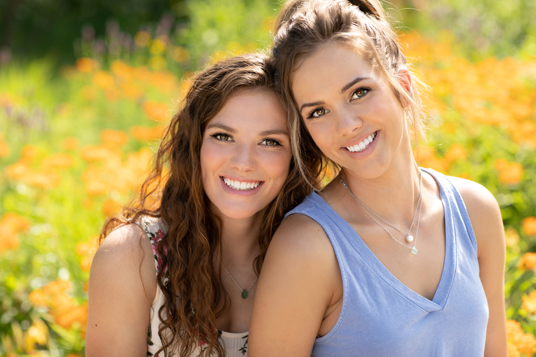 Sisters hugging in together in front of a field of amazing orange flowers in Colorado