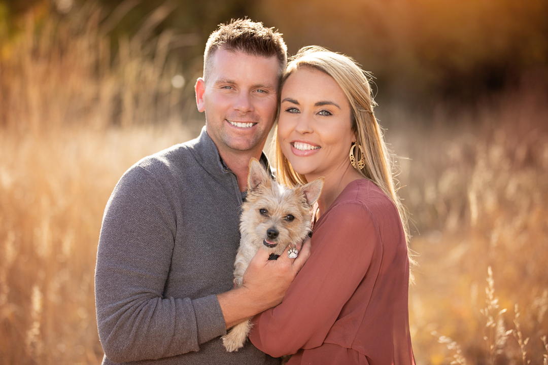 Engagement portrait of a couple and their little dog in a field in the fall season