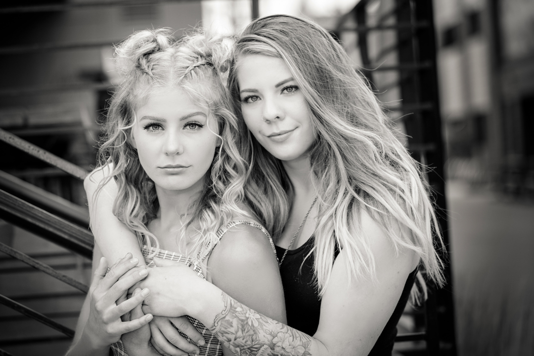 Sister photo taken in black and white of the sisters hugging into each other with a serious expression in Old Town Ft. Collins