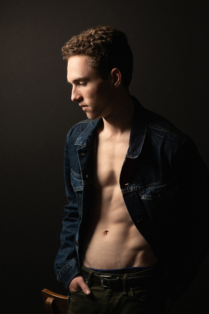 Dark portrait of a male model wearing a jean jacket, showing off his abs