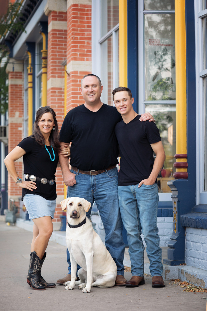 A mom and a dad with their teenage son and dog posing for family photos on a downtown street in Fort Collins, Colorado