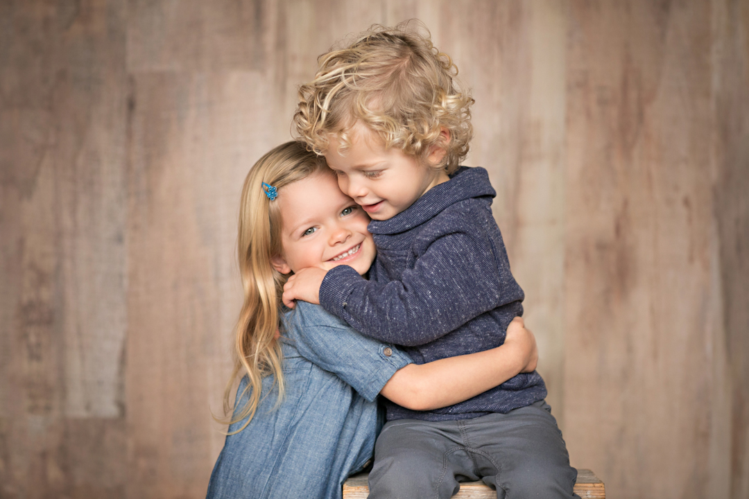 Studio portrait of a brother and sister hugging each other with a wood background