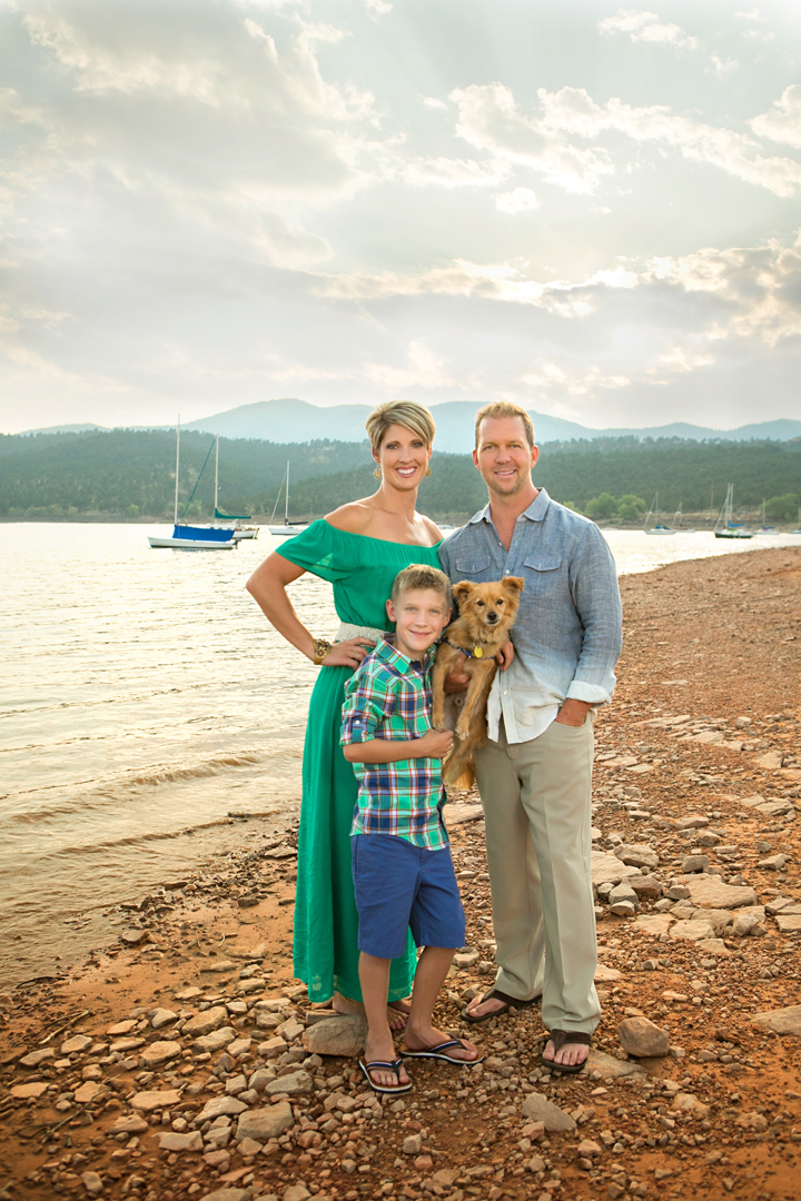 Family photo session taken at Carter Lake of a family with a little dog in front of Carter Lake with boats on the water in the background