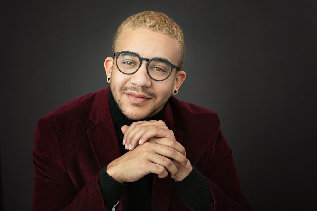 Studio business headshot of a young man pursuing theater wearing a red corduroy jacket and round glasses