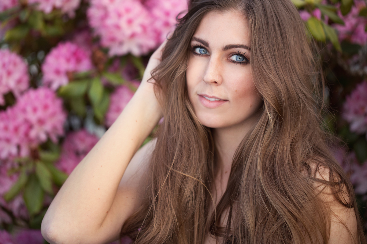 Portrait taken during a personal branding session of a young beautiful photographer with stunning blue eyes in front of bunches of pink flowers