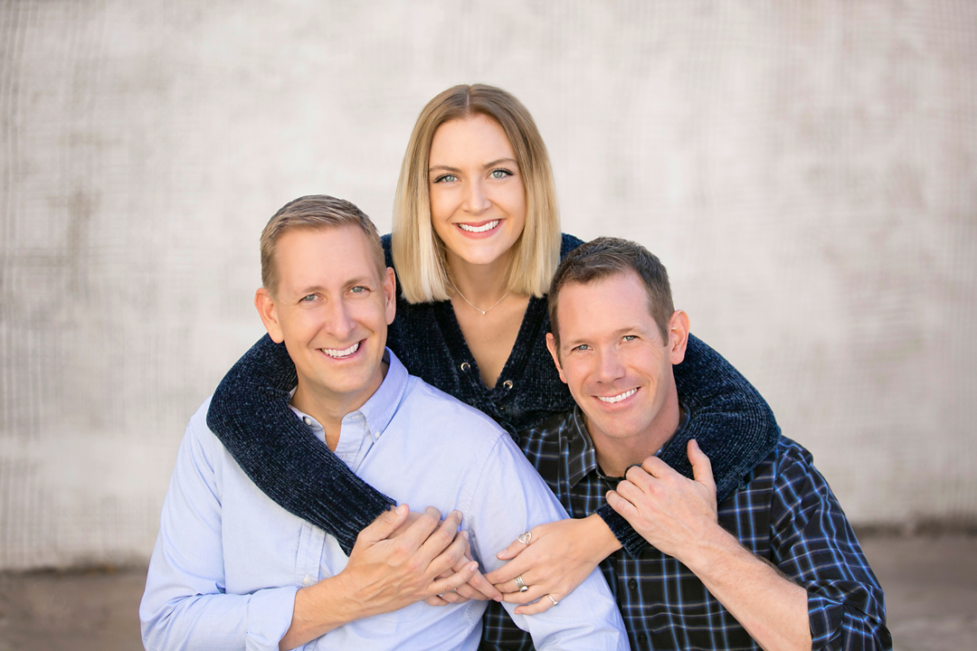 Adult sister with her two adult brothers posing for family photos in front of a grey concrete background
