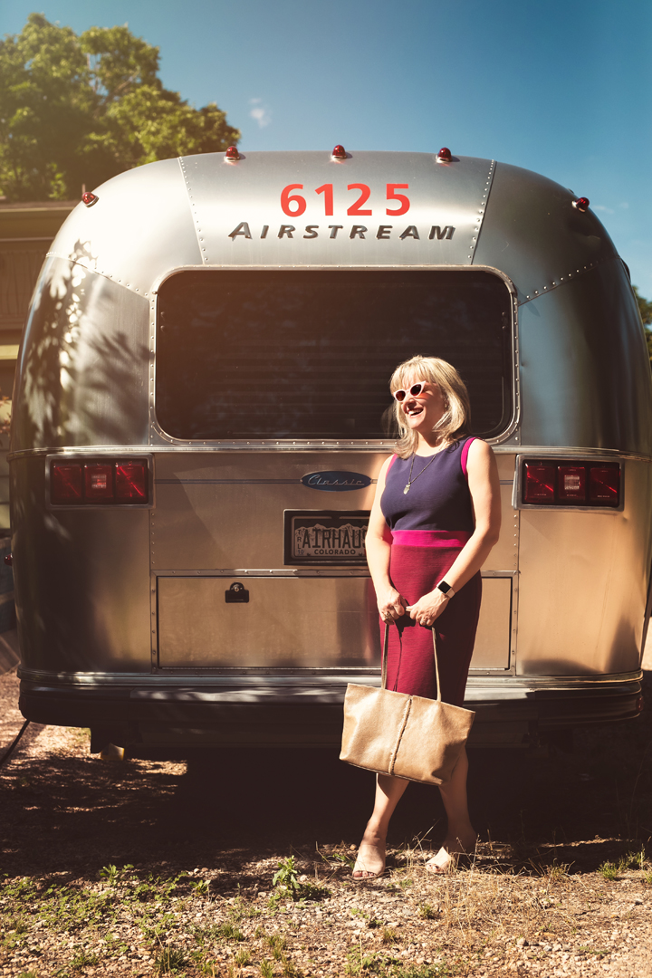 Woman in vintage outfit with cat eye sunglasses standing behind her Airstream in Colorado