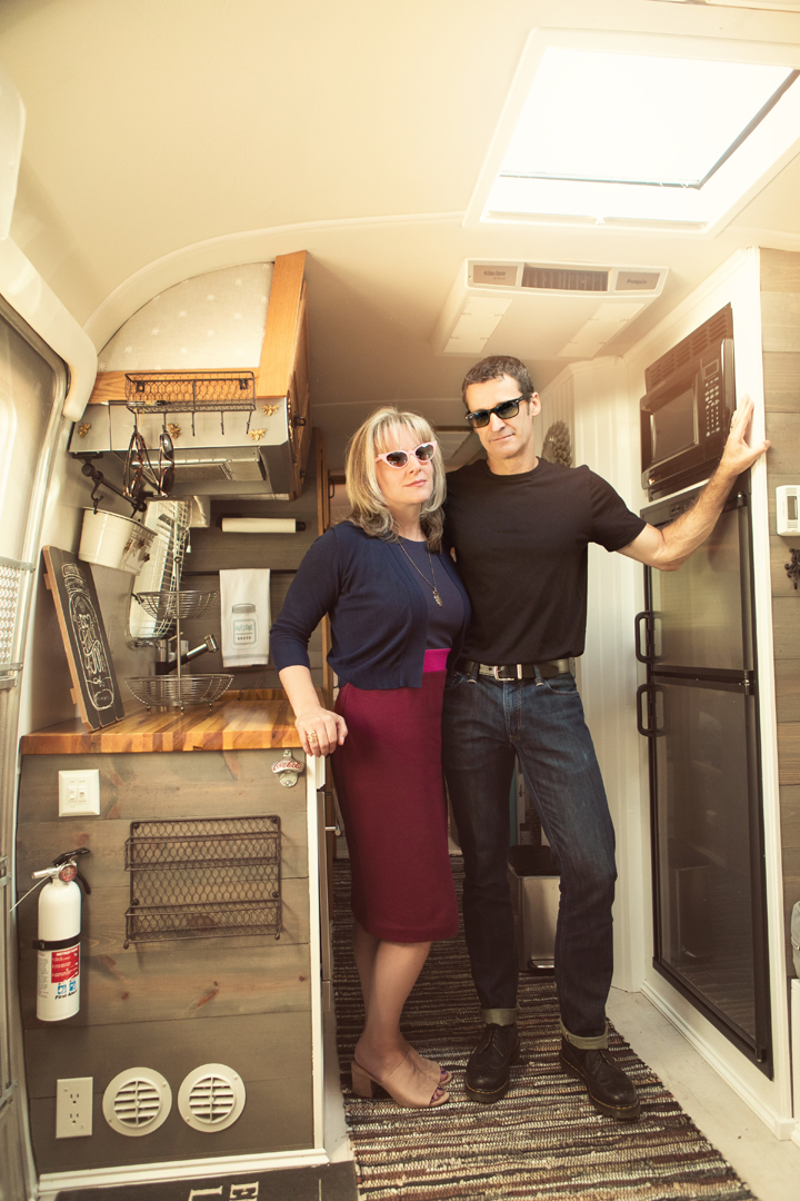 portrait of a couple in their Airstream in Fort Collins.  They are standing in the kitchenette wearing sunglasses and the shot has a vintage feel