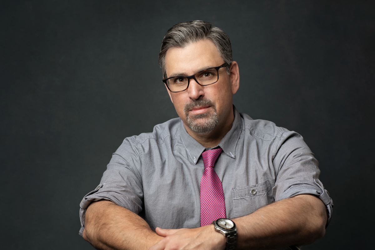 Studio portrait taken of a man wearing a gray shirt and pink tie for an updated business headshot