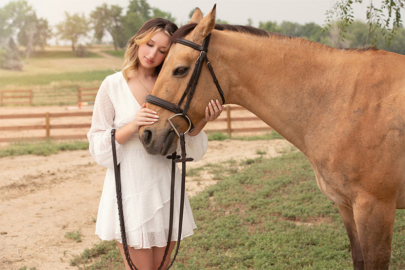 A girl poses angelically with her head resting on her horses forehead.