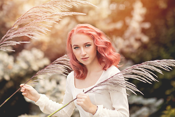 Edgy-looking senior girl with blush pink coral hair is surrounded by magical pampas grass in a field in Northern Colorado 