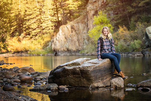 Sweet outdoorsy senior girl smiling while sitting on top of a rock in the Poudre Canyon for her senior portraits