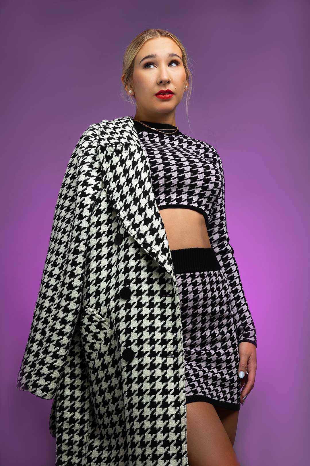 A blonde high school senior model in a high-fashion outfit poses in front of a bright purple background in the studio of Desirée Suchy, the photographer of Photography by Desirée