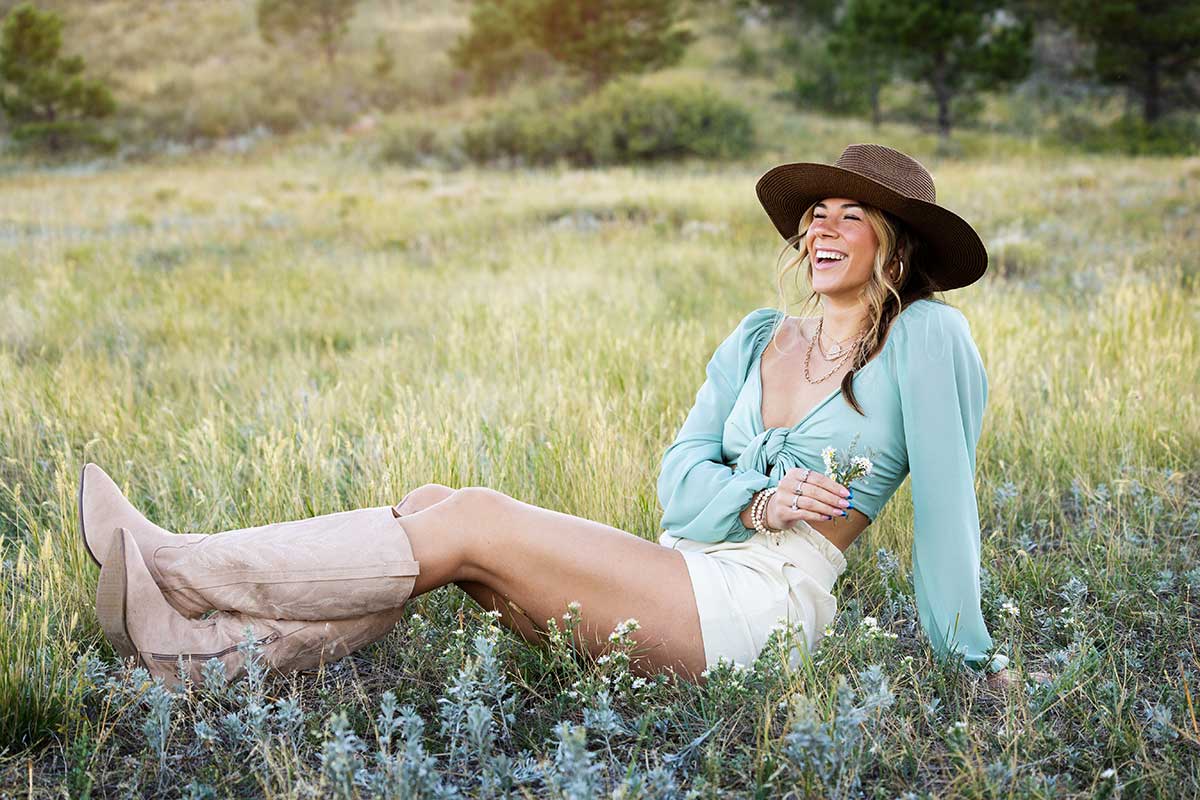 Girl in a western boho outfit sitting comfortably while laughing and posing for a senior portrait in Denver Colorado