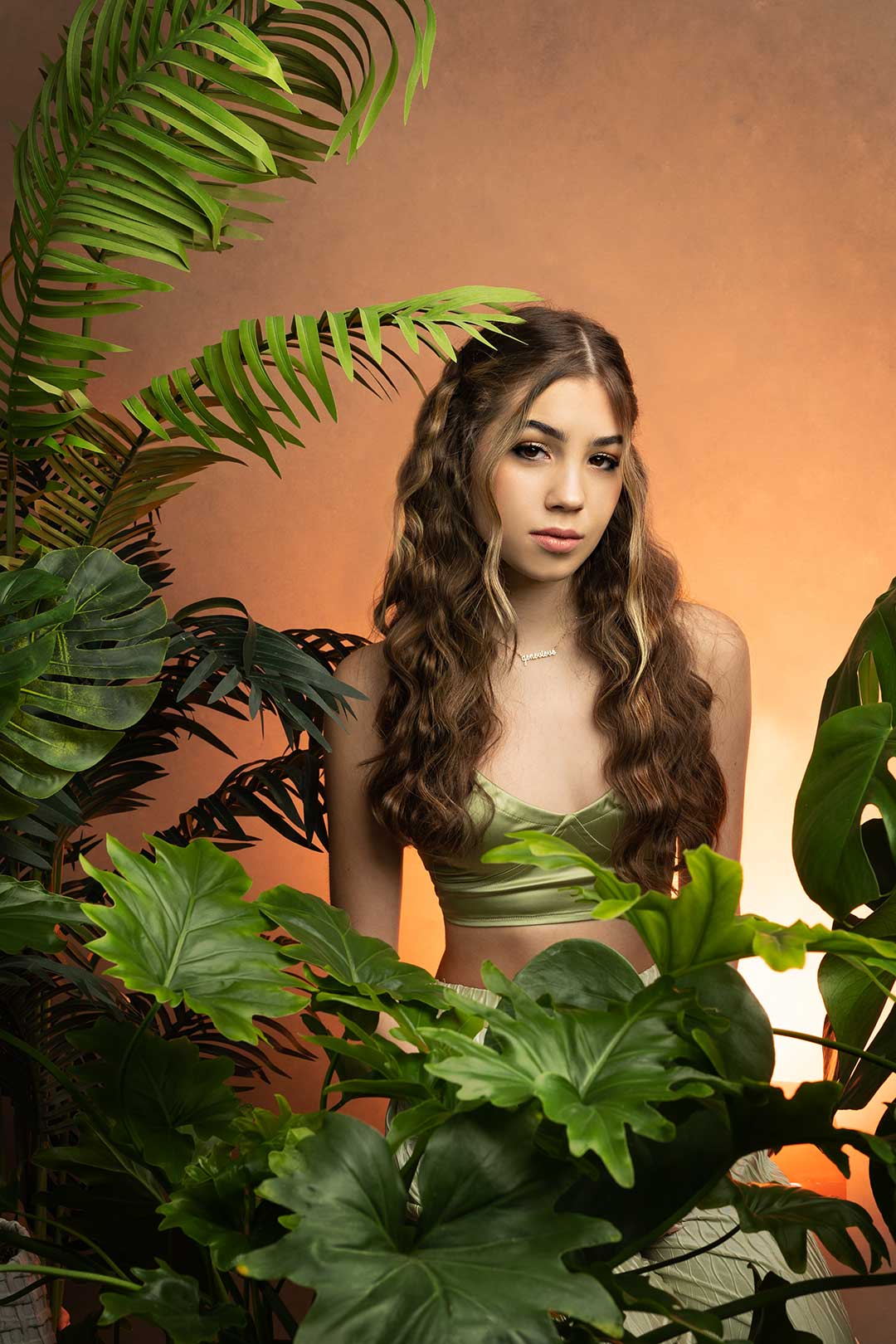 Natural Senior Portrait of a girl standing among some tropical leaves on a coral backdrop in Fort Collins Colorado