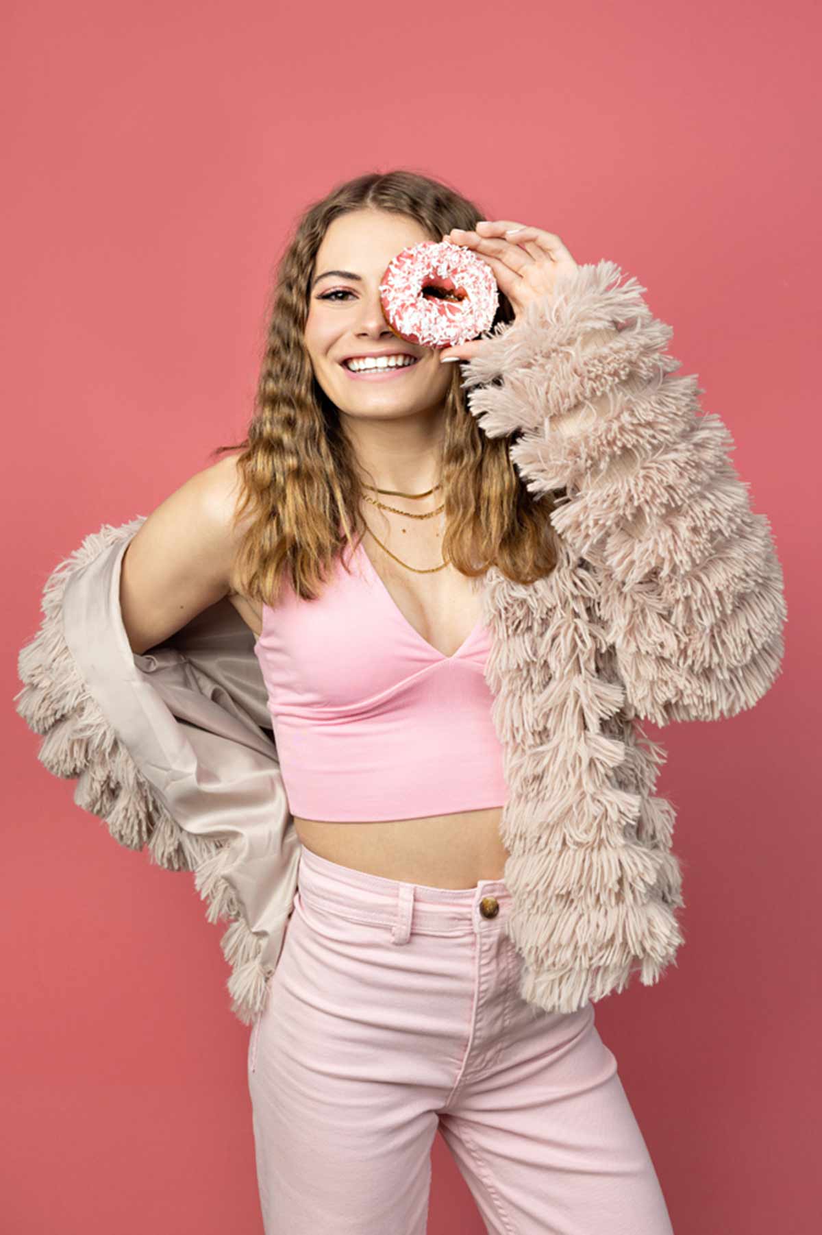 A monochromatic themed photo of a girl in all pink on a pink background holding a cute sprinkled donut as a prop for the PBD Model Team