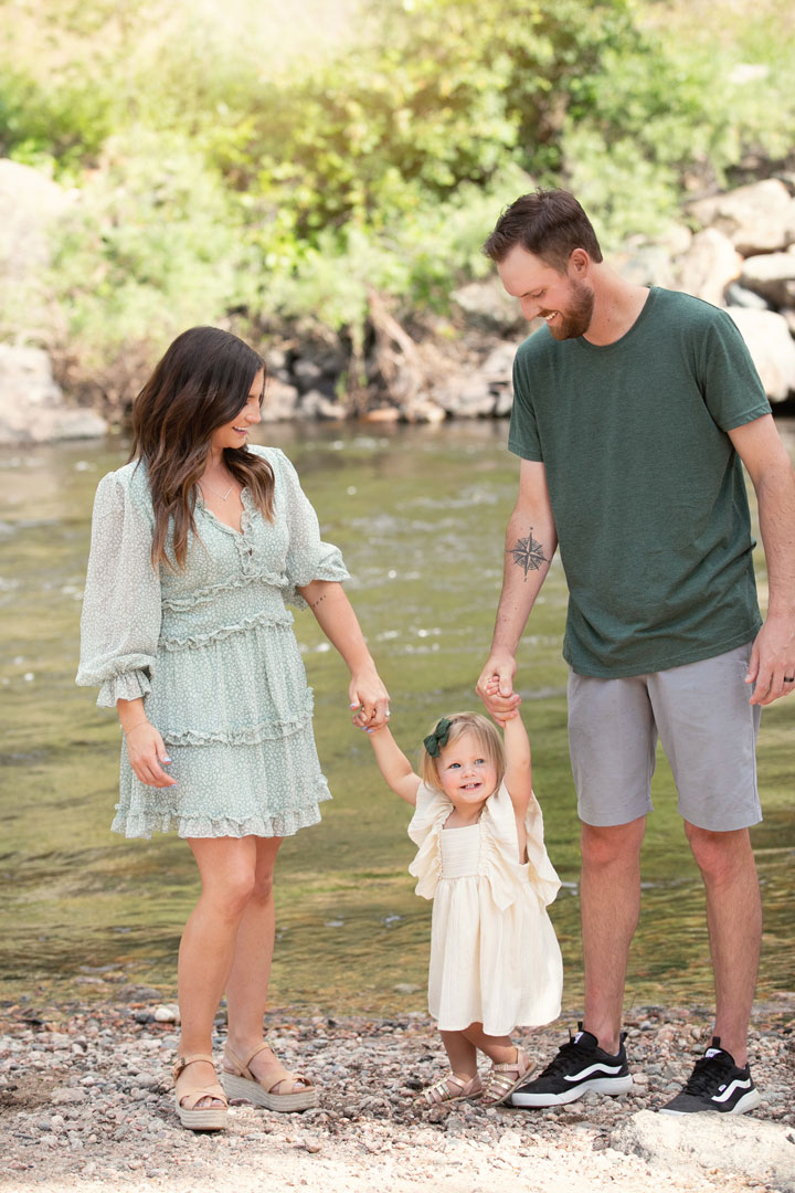 Family photo of mom, dad, and young daughter playing near the Cache la Poudre River shot by Photography by Desiree