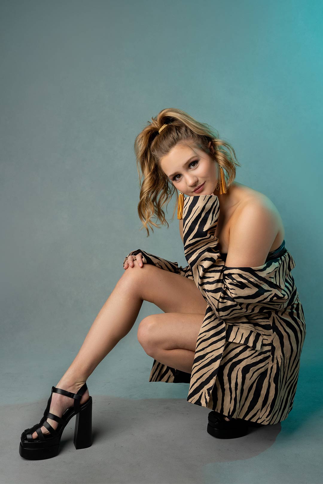 Edgy high school senior portrait of a girl in in a zebra print trench coat on a teal colored studio backdrop