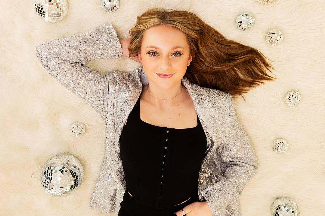 High school senior girl laying on a fur rug surrounded by disco balls as a part of Photography by Desirée's model team's Christmas shoot