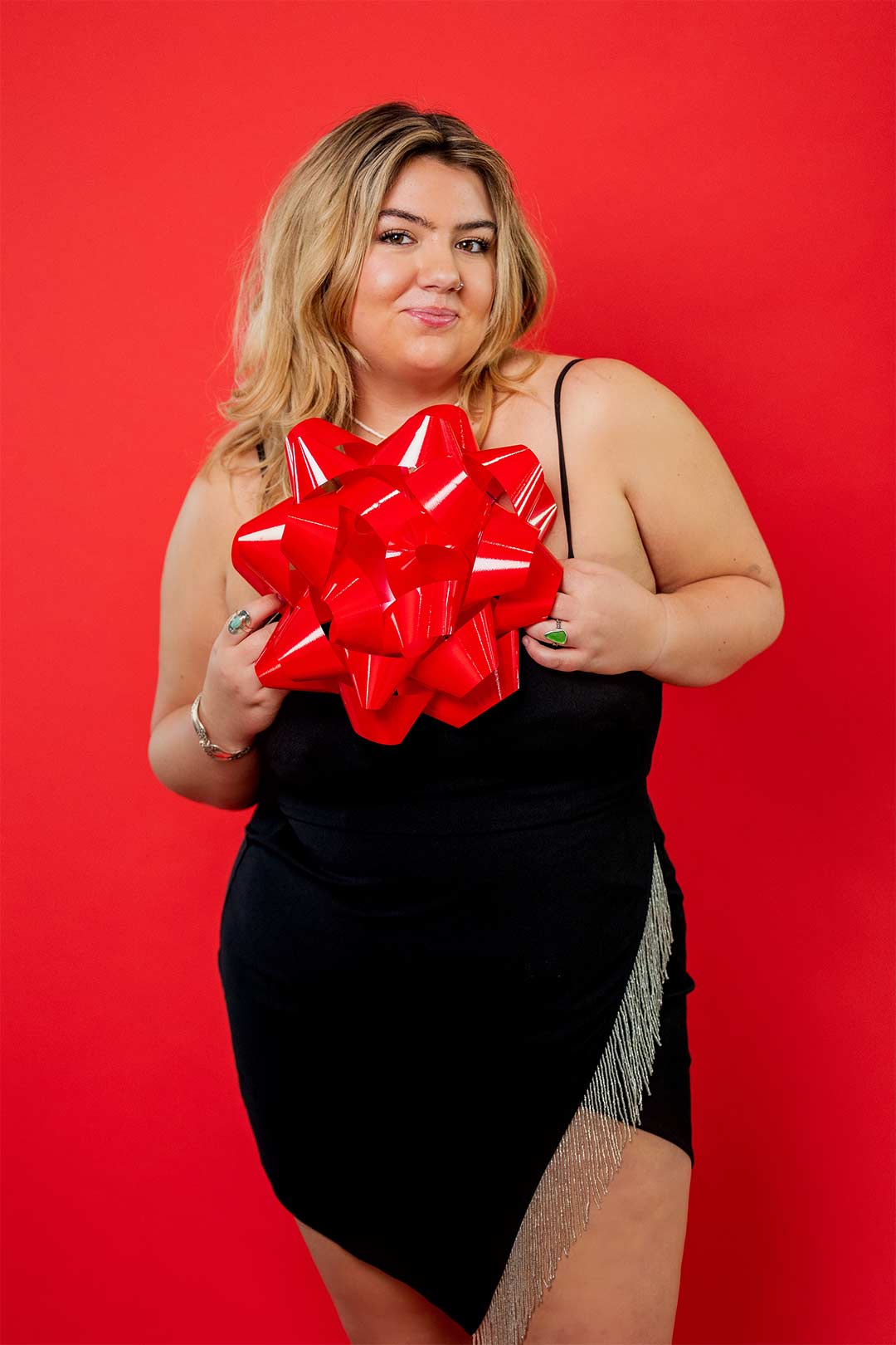 Young high school senior girl posing with a giant red bow on a red studio backdropin the holiday themed photoshoot of the Photography by Desirée senior model team