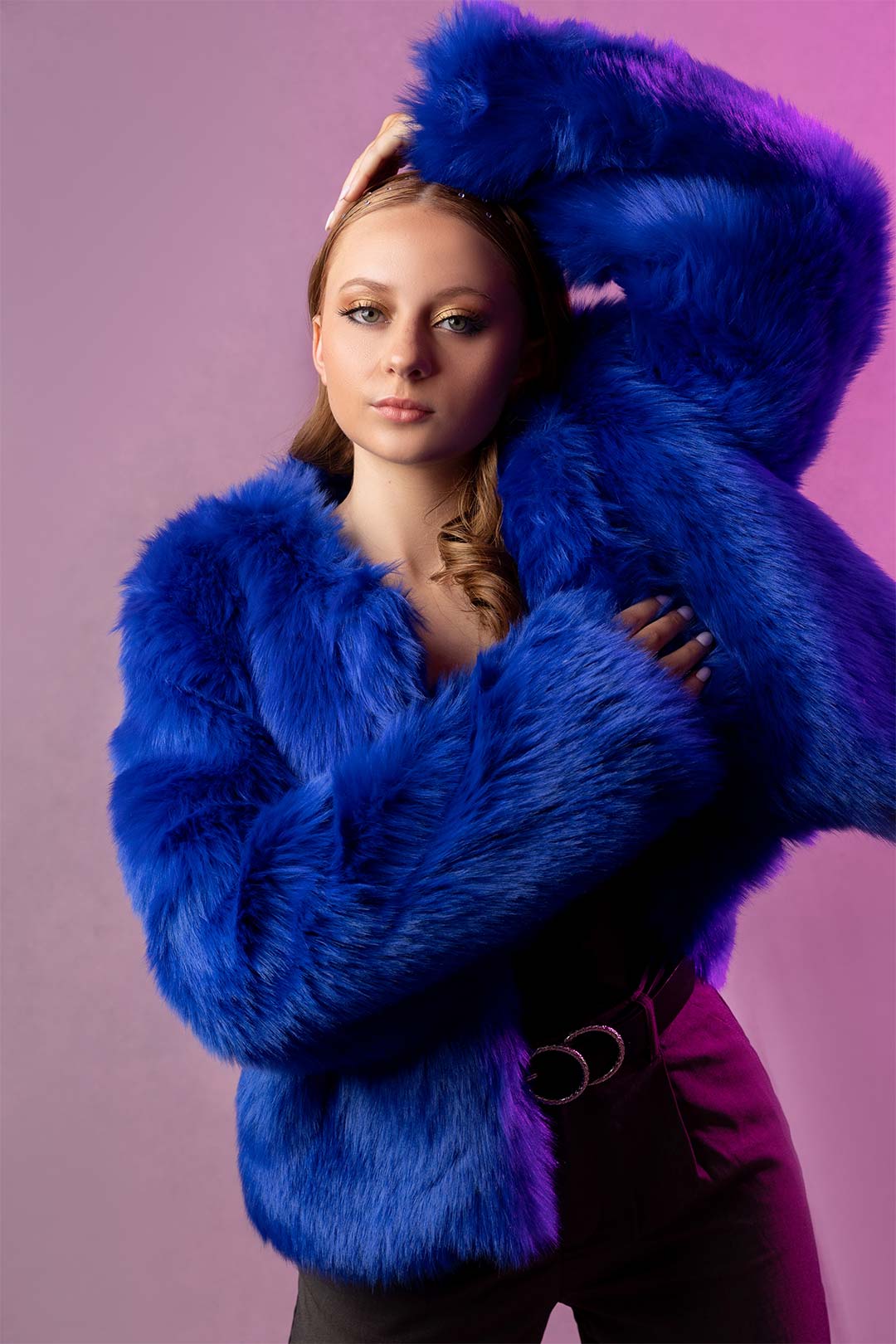 Dramatic studio portrait of a high school senior girl wearing a blue fur coat in front of a purple background