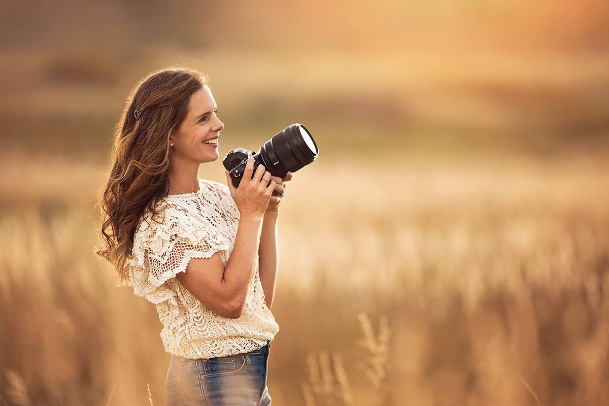 Soft, dreamy lifestyle portrait of photographer with her camera in a blurry warm field